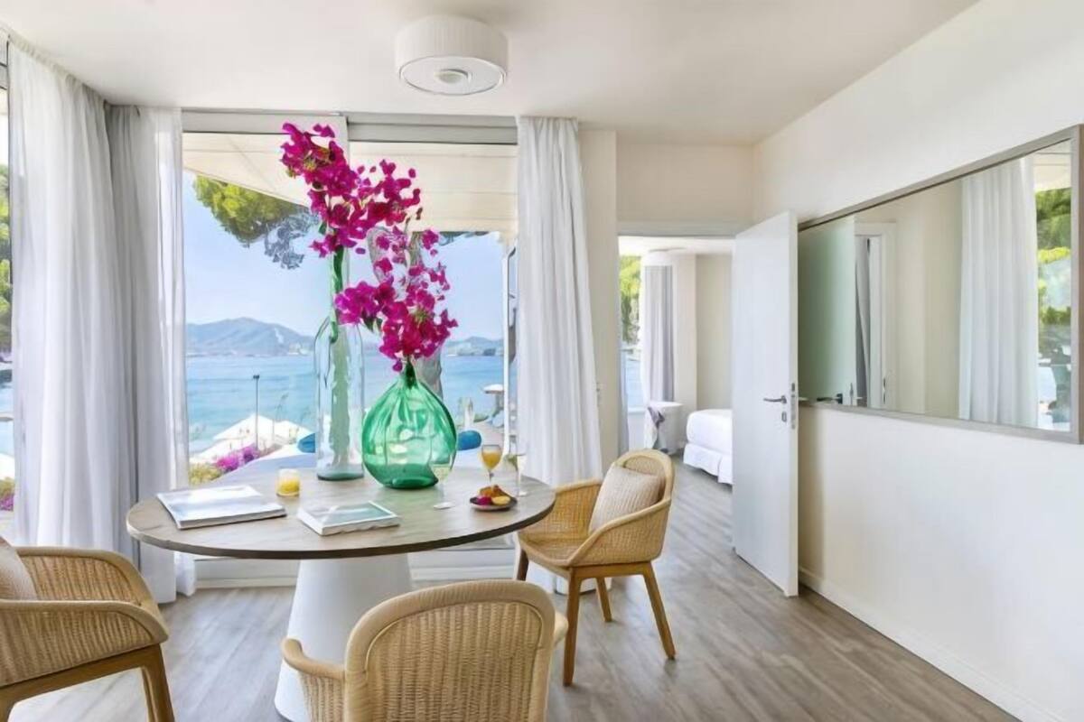 Une chambre moderne avec une table ronde, des chaises en osier et une vue sur la mer.