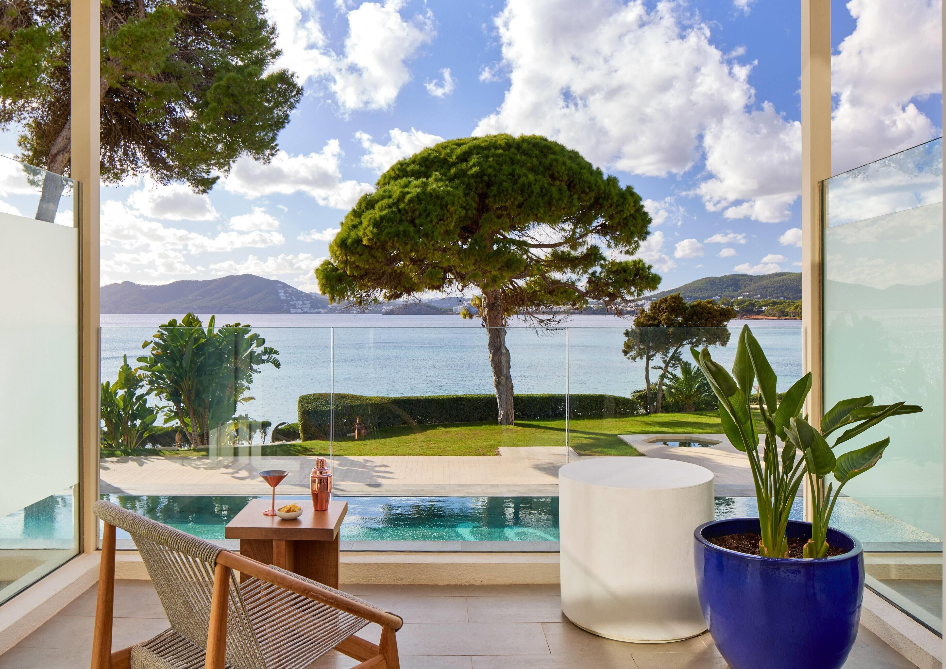 A modern balcony with a clear view of a lake, a well-maintained lawn, and a large tree.