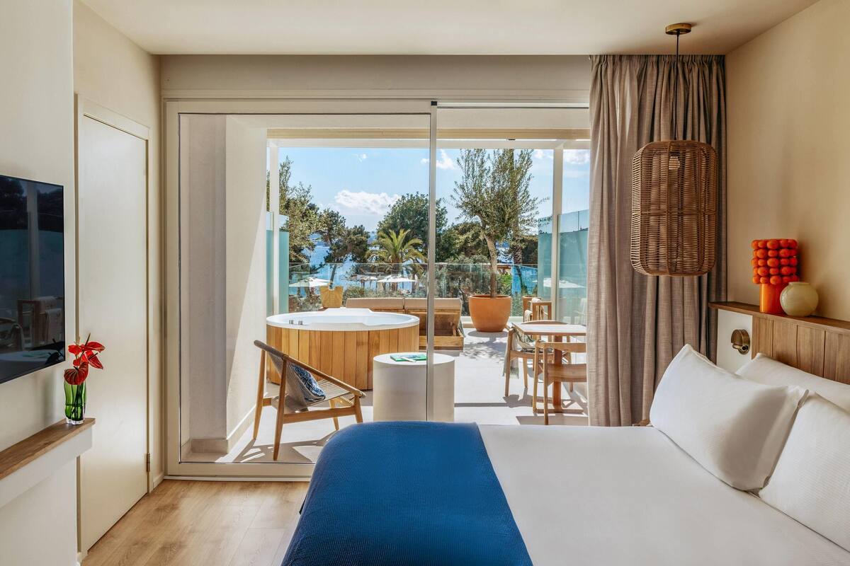 Une chambre d’hôtel comprenant un lit, une télévision, un balcon avec vue sur la mer et un coin repas.