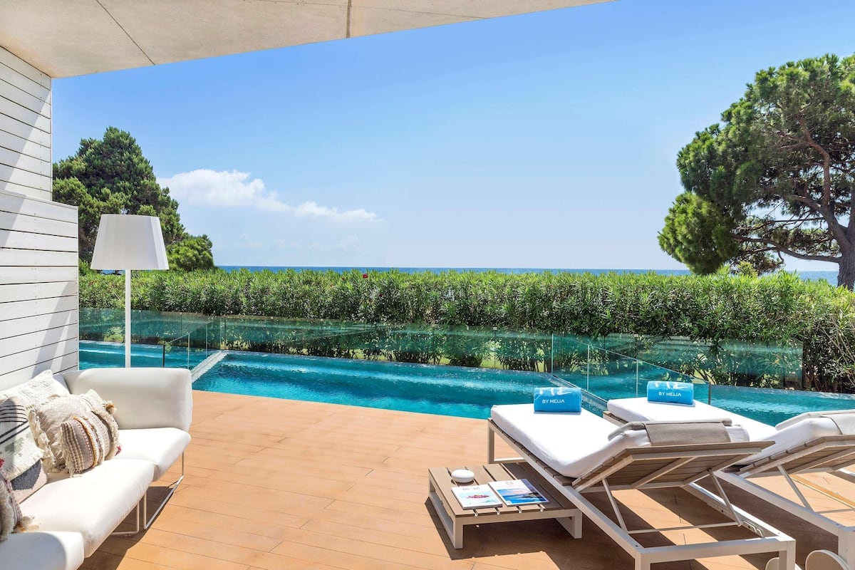 Un espace aménagé au bord de la piscine, avec un canapé blanc, des chaises longues et une piscine entourée de parois en verre.