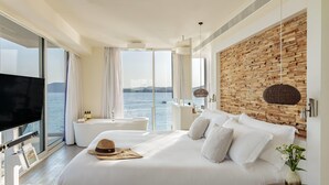 Ein modernes Schlafzimmer mit einem großen Bett, einem Fernseher, Meerblick, einer Holzwand und einem Badezimmer mit einer Badewanne.