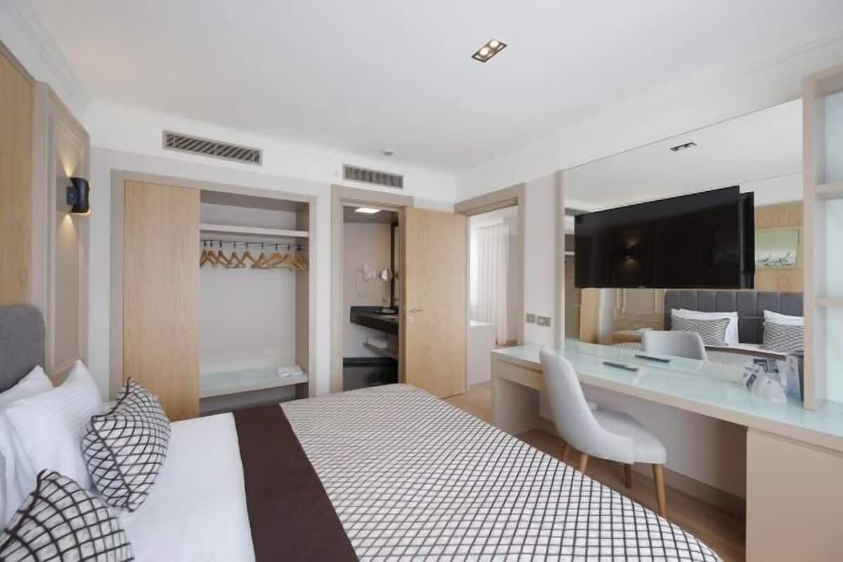 A hotel room with a bed, a desk, a chair, a TV, and a wardrobe.