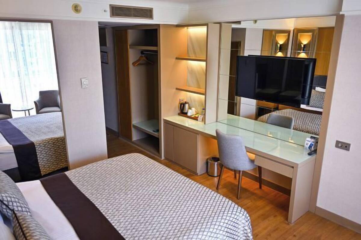 A hotel room with a bed, a desk, a chair, a television, and a wardrobe.