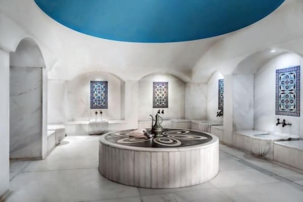A circular marble fountain with a central sculpture, surrounded by white marble walls and arches, with patterned windows. - Porto Bello Hotel Resort & Spa (Antalya)