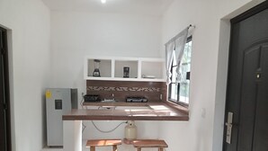 A compact kitchen with a countertop, a built-in stove, a sink, and a refrigerator. There are two wooden stools under the counter. - Apartamento #3 (Macario Gómez)