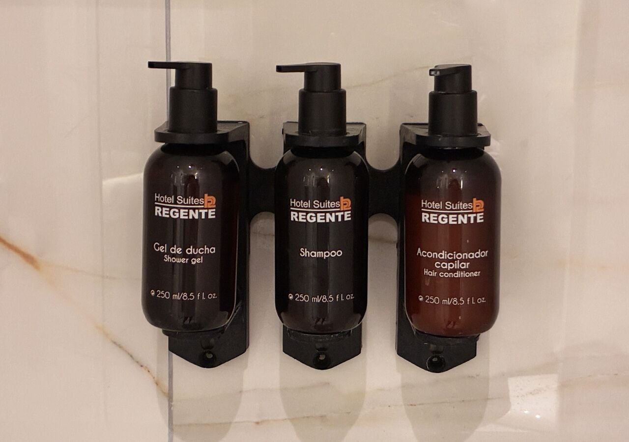 Trois flacons de produits de la gamme Hotel Suites REGENTE : gel douche, shampooing et après-shampooing, chacun doté d’un distributeur à pompe et portant une étiquette indiquant le volume.