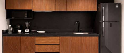 A modern kitchen with wooden cabinets, a black countertop, a built-in microwave, a coffee maker, and a refrigerator.