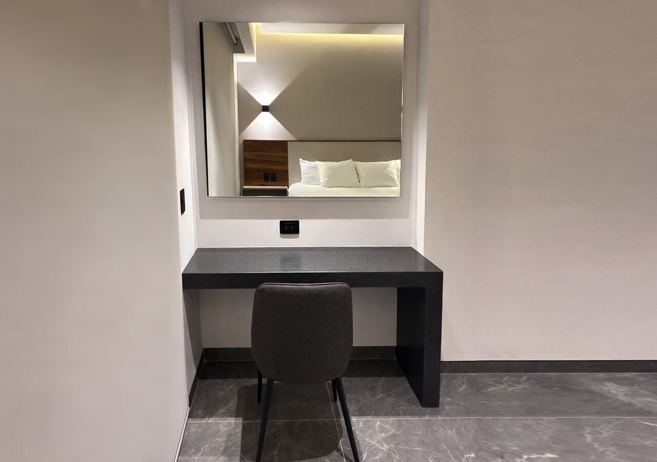Une chambre moderne avec un bureau sombre, une chaise et un grand miroir qui reflète un lit.
