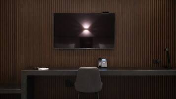 A modern room with a dark wood panel wall, a flat-screen TV mounted above a dark desk, a telephone, and a chair.