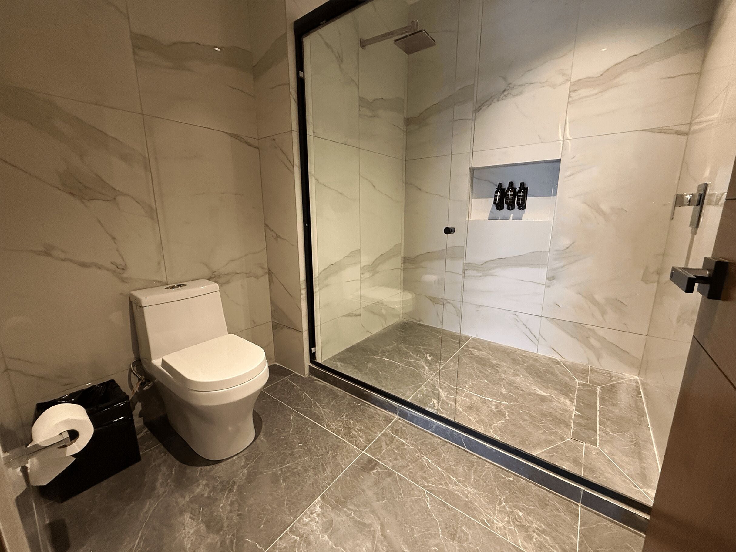 A modern bathroom with a toilet, a glass-enclosed shower, and a marble floor.