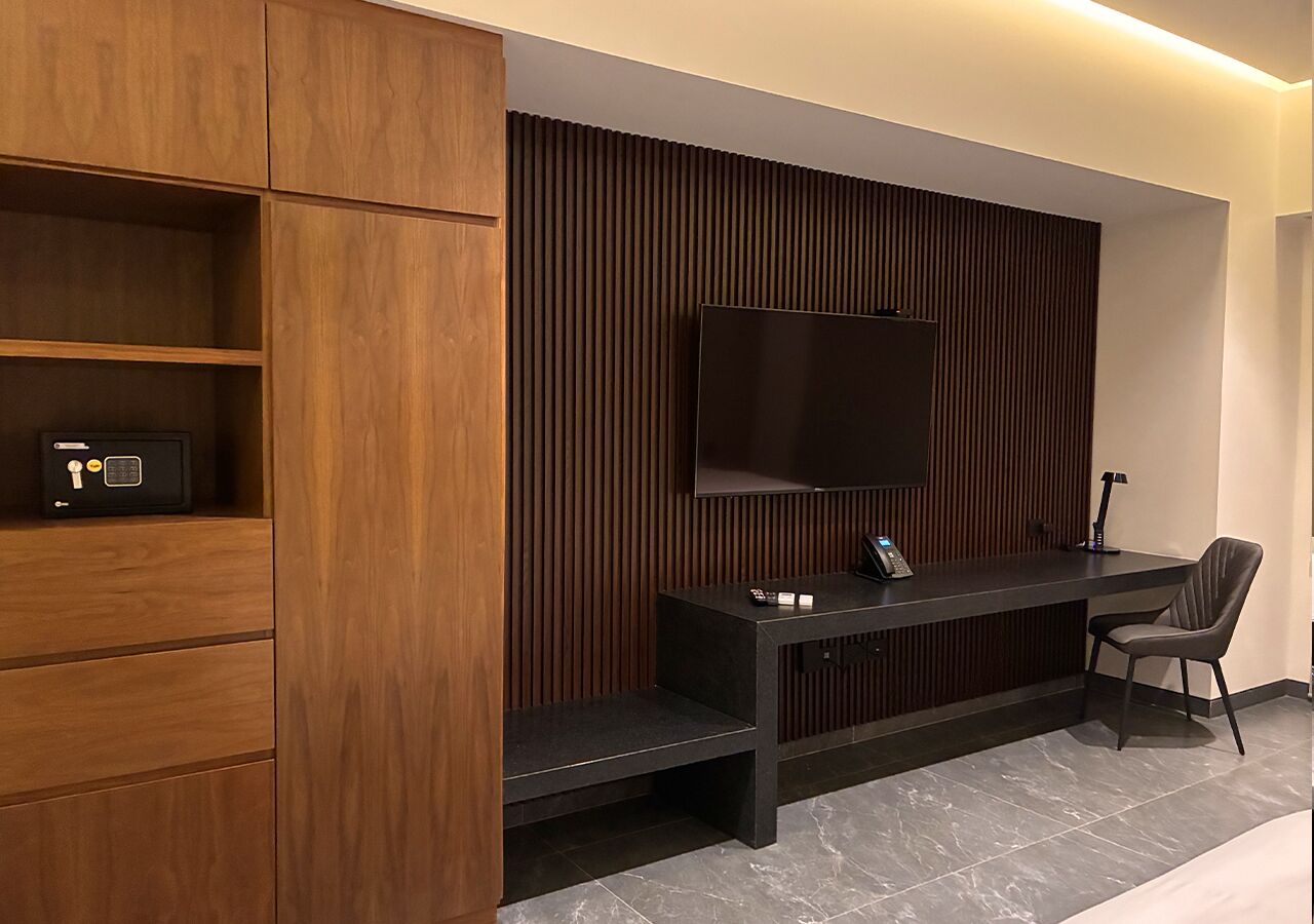 Een moderne kamer met een houten kast, een flatscreen televisie aan de muur, een bureau met stoel en een telefoon.