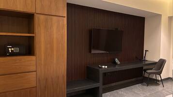 Een moderne kamer met een houten kast, een flatscreen televisie aan de muur, een bureau met stoel en een telefoon.