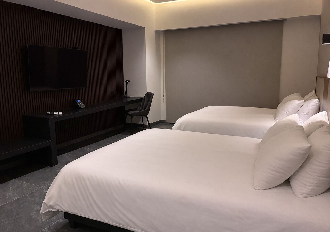 A hotel room with two beds, a TV mounted on the wall, and a desk with a chair.