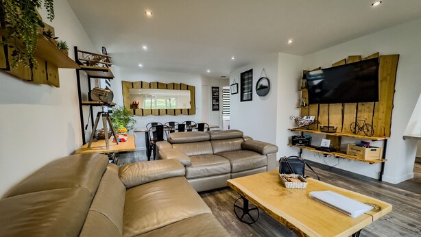 Un salon moderne comprenant un canapé d’angle, un coin repas et un téléviseur fixé au mur, qui est en bois.