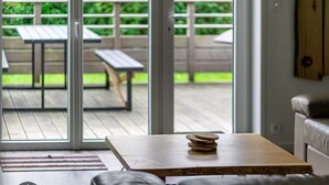 Una mesa de madera con posavasos apilados y vistas a un patio exterior con un banco y una mesa.