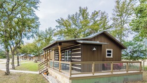 A lodge with a porch, a staircase, and a fenced deck area. - 6) Texas Pride  at Vineyard Trail Cottages (Fredericksburg)