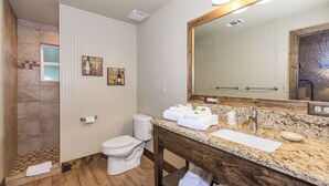 A bathroom with a wooden vanity, a large mirror, a toilet, and two wall-mounted towel racks. - 6) Texas Pride  at Vineyard Trail Cottages (Fredericksburg)