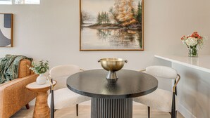 Ein Essbereich mit einem runden Tisch, zwei Stühlen, einer Blumenvase und einem gerahmten Gemälde an der Wand.