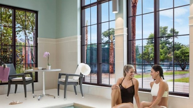 Ein Poolbereich im Innenbereich mit zwei Personen am Pool, einem kleinen Tisch mit einer Vase und Stühlen.