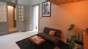 Uma sala de estar aconchegante com um sofá marrom, uma mesa de centro com revistas, um vaso de plantas e uma obra de arte emoldurada na parede.