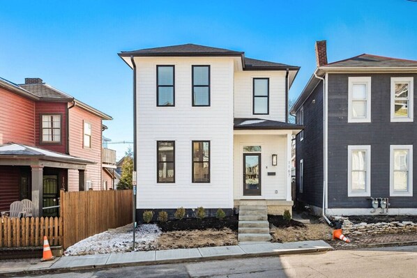 A two-story residential building with a white exterior, a front porch, and a small front yard.