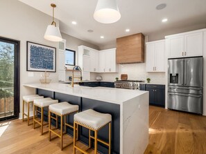 A modern kitchen with a central island, bar stools, stainless steel appliances, and a large window. - High End New Build, Rooftop Hot Tub, City Views! (Columbus)