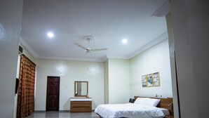 A bedroom with a bed, a dresser, a ceiling fan, and a door. - Private Home Lodge (Accra)