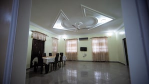 A spacious room with a high ceiling, a ceiling fan, a dining table with chairs, and a door. - Private Home Lodge (Accra)