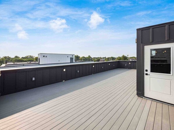 A rooftop deck with a wooden floor, a black railing, and a white door. - New Build, Downtown Views, next to NCH (Columbus)