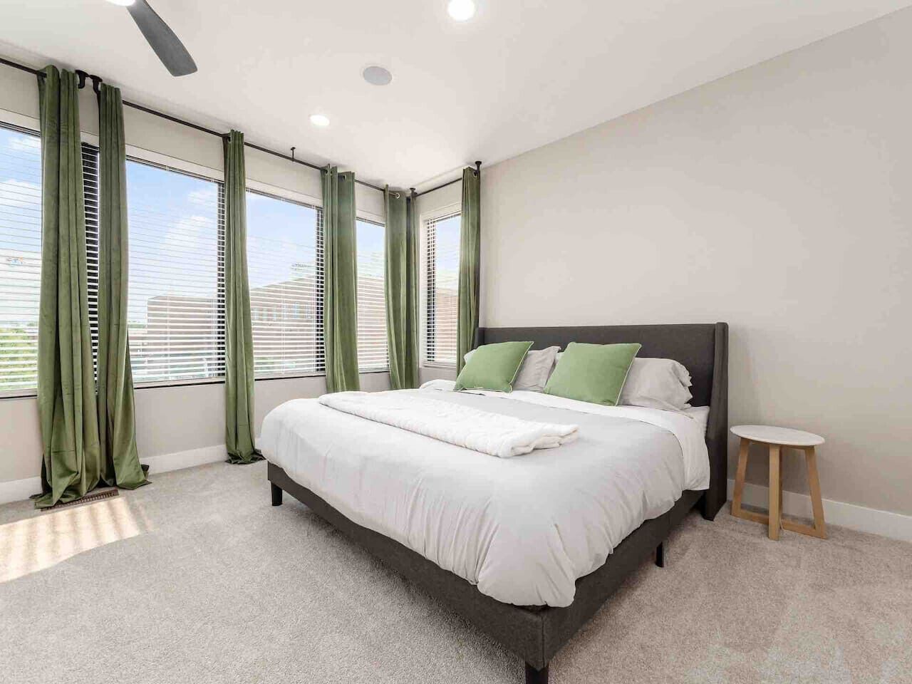A modern bedroom with a large bed, green curtains, and a small stool.