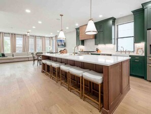 A modern kitchen with a central island, bar stools, and green cabinetry. - New Build, Downtown Views, next to NCH (Columbus)