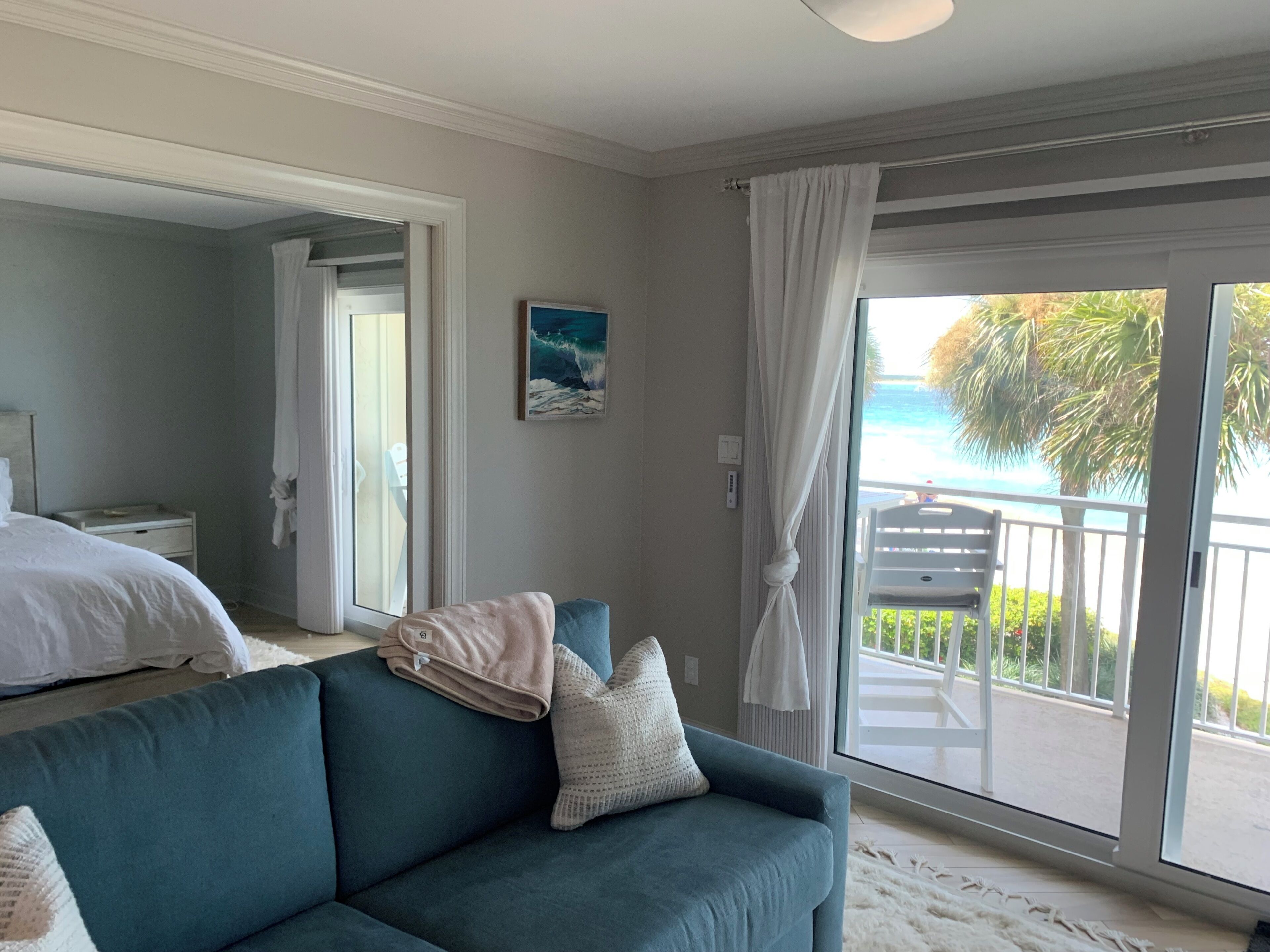 A bedroom with a large bed, a blue sofa, and a balcony with a view of the ocean.