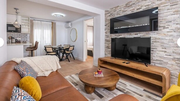 Una sala de estar moderna con un sofá, una mesa de centro y un televisor montado en una pared de piedra.