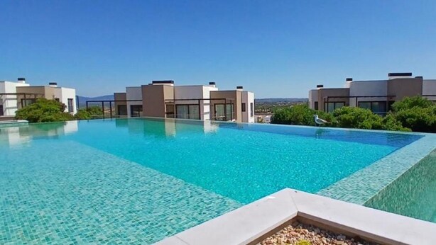 Ein moderner Pool mit klarem, blauem Wasser, umgeben von zeitgenössischer Architektur und Grünflächen.