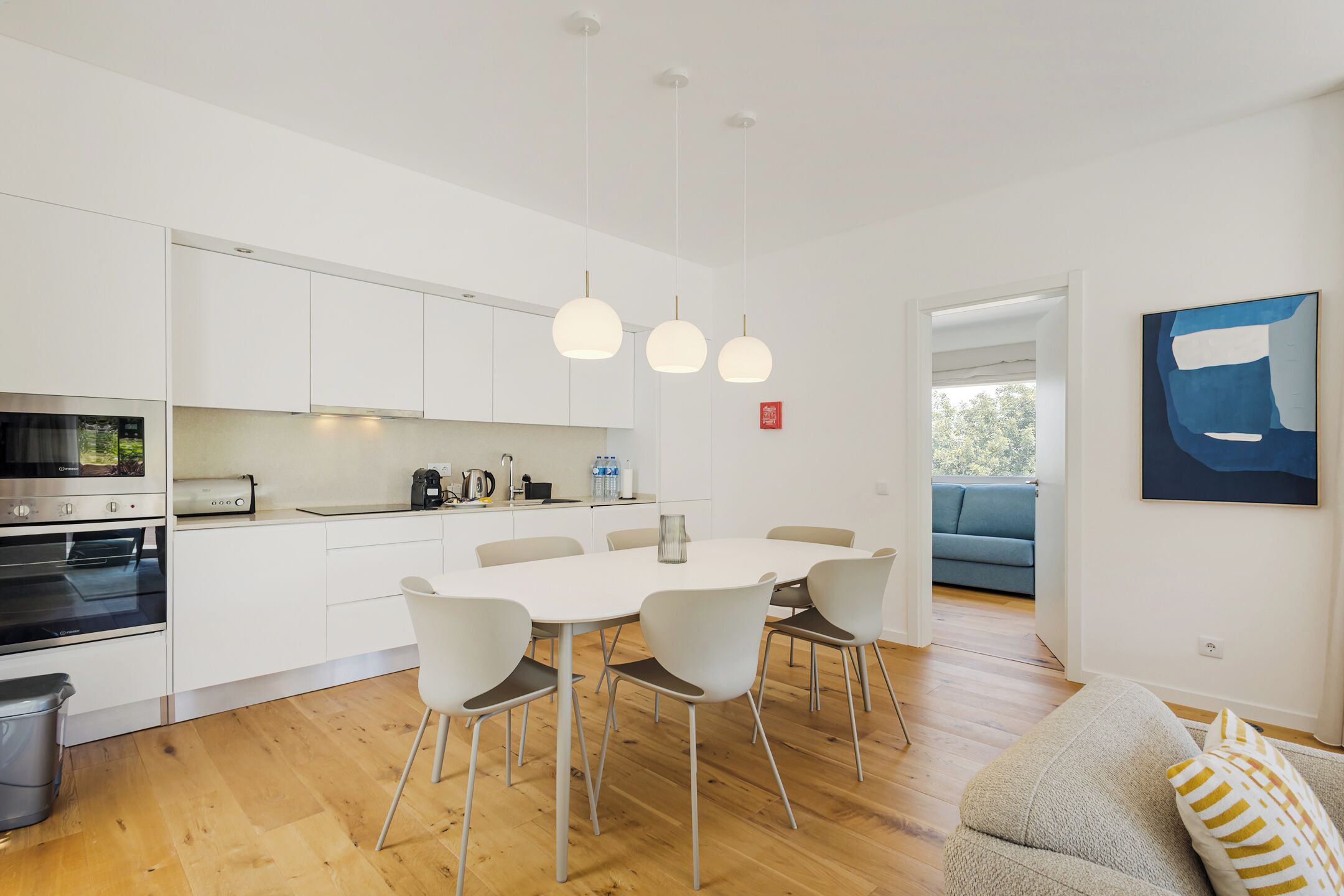A modern kitchen with white cabinets, a dining table with chairs, and pendant lights.