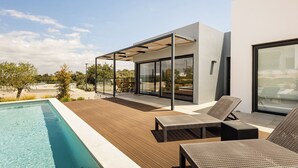 Ein moderner Poolbereich im Freien mit Holzterrasse, Liegestühlen und einer glasgeschlossenen Terrasse.