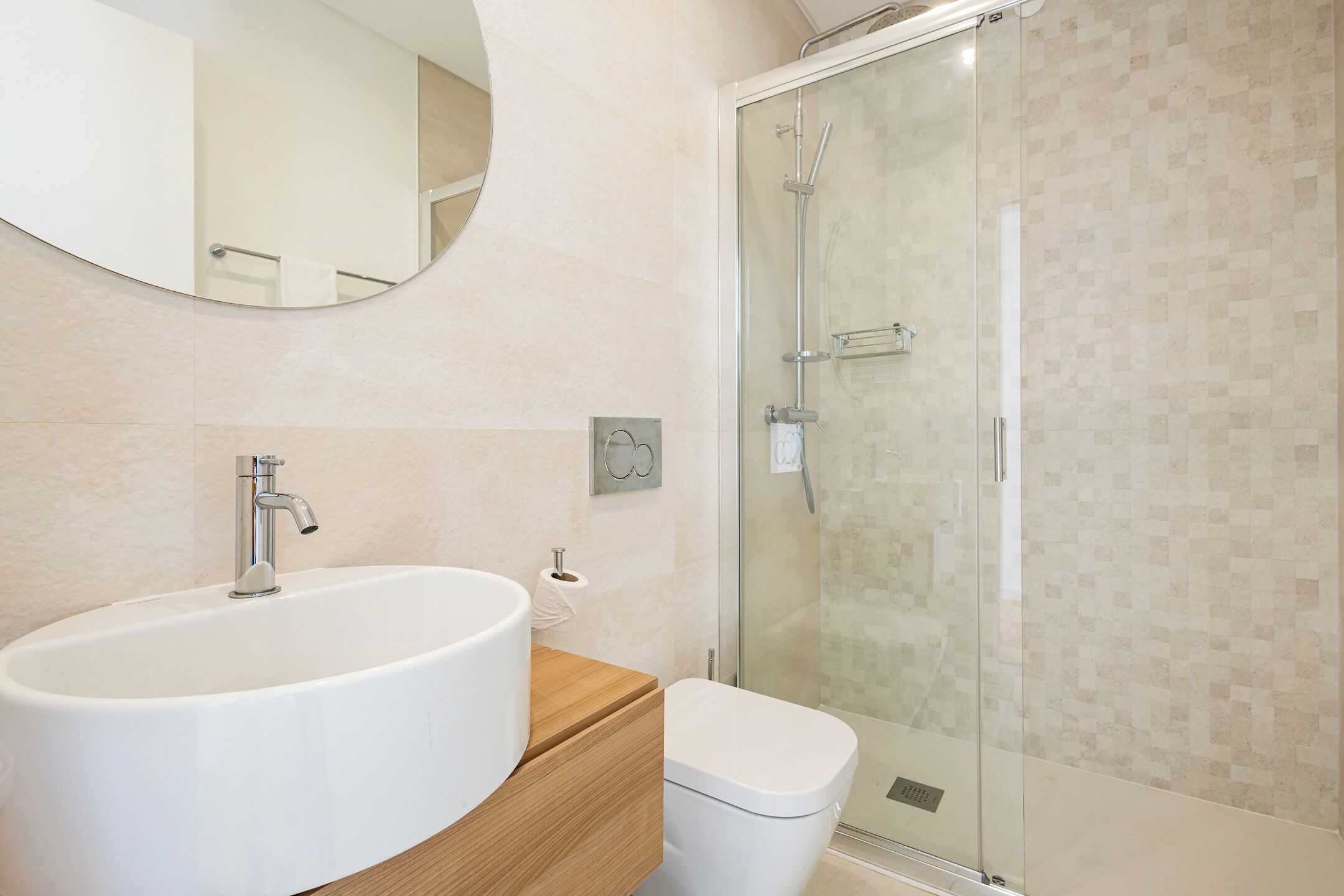 Une salle de bain moderne avec un grand lavabo blanc, un meuble-lavabo en bois, des toilettes et une douche à parois de verre.