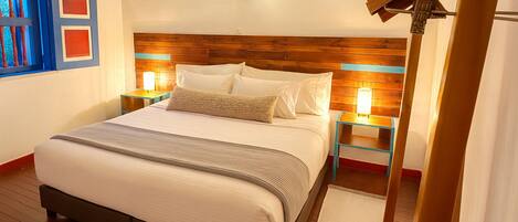 A neatly made bed with a wooden headboard, two bedside tables with lamps, a window with blue frames, and a wooden floor.