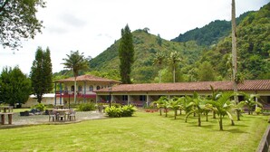 A building with a red-tiled roof, surrounded by a well-maintained lawn with palm trees, and a mountainous backdrop. - Dreamer Cocora (Salento)
