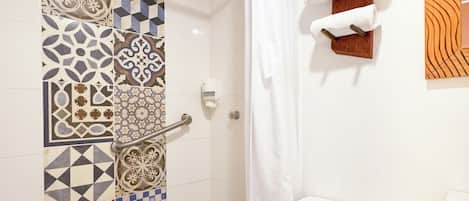 A bathroom with patterned tiles, a white toilet, a shower with a white curtain, and towels on a wooden rack.