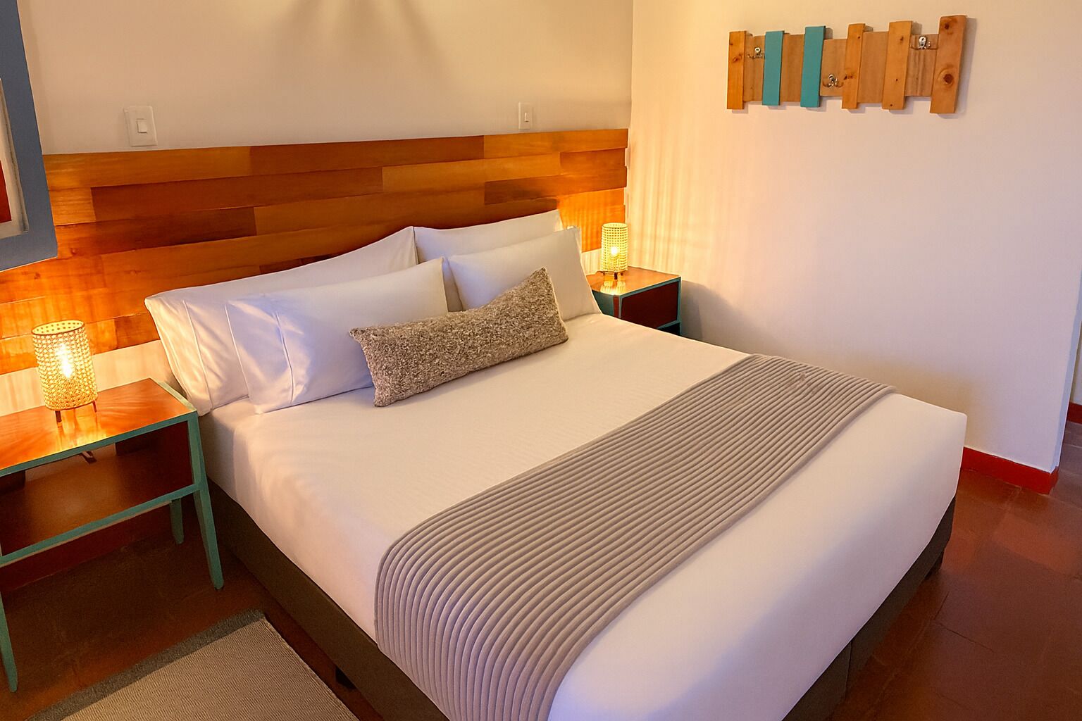 A neatly made bed with white linens and a beige throw, a bedside table with a lamp, and a wooden headboard.