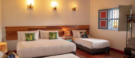 A hotel room with two beds, a wooden headboard, wall-mounted lights, and a window with red frames.