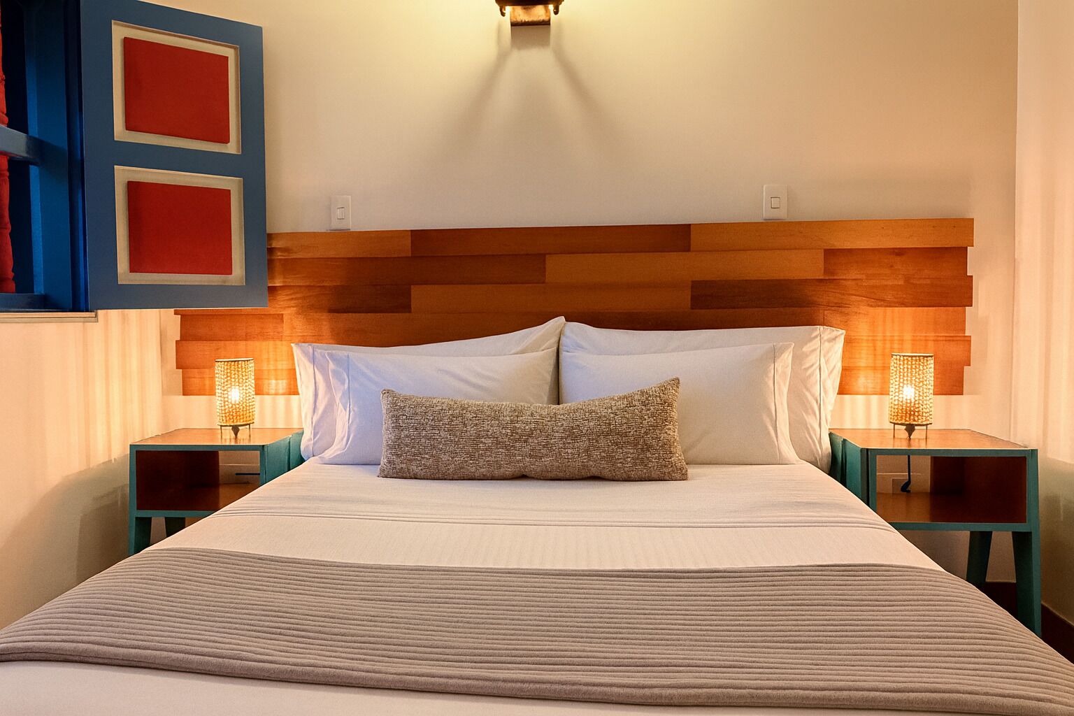 A bedroom with a wooden headboard, two bedside tables with lamps, a bed with white linens, and a textured throw pillow.