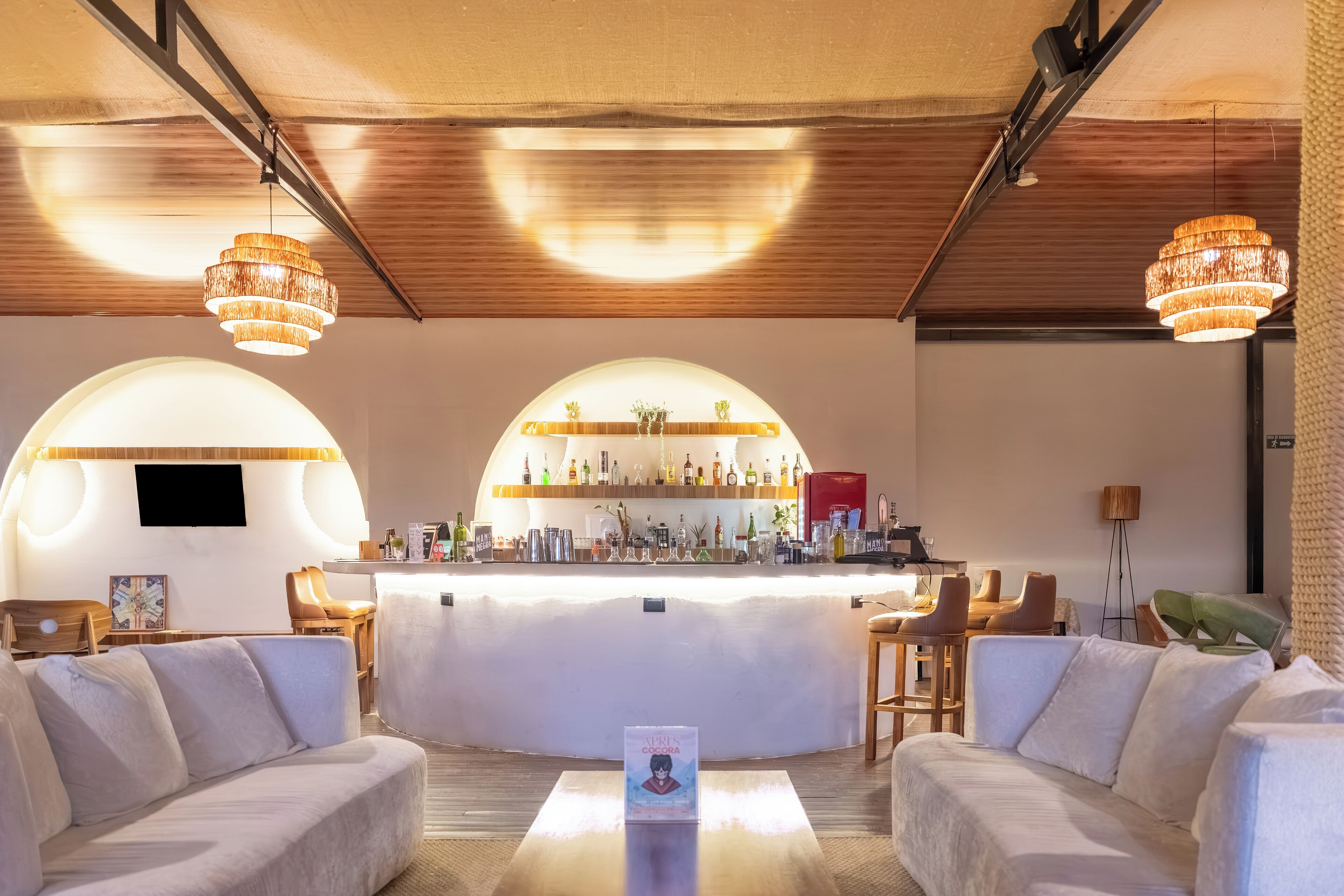 A modern bar area with a curved counter, bar stools, and a seating area with sofas.