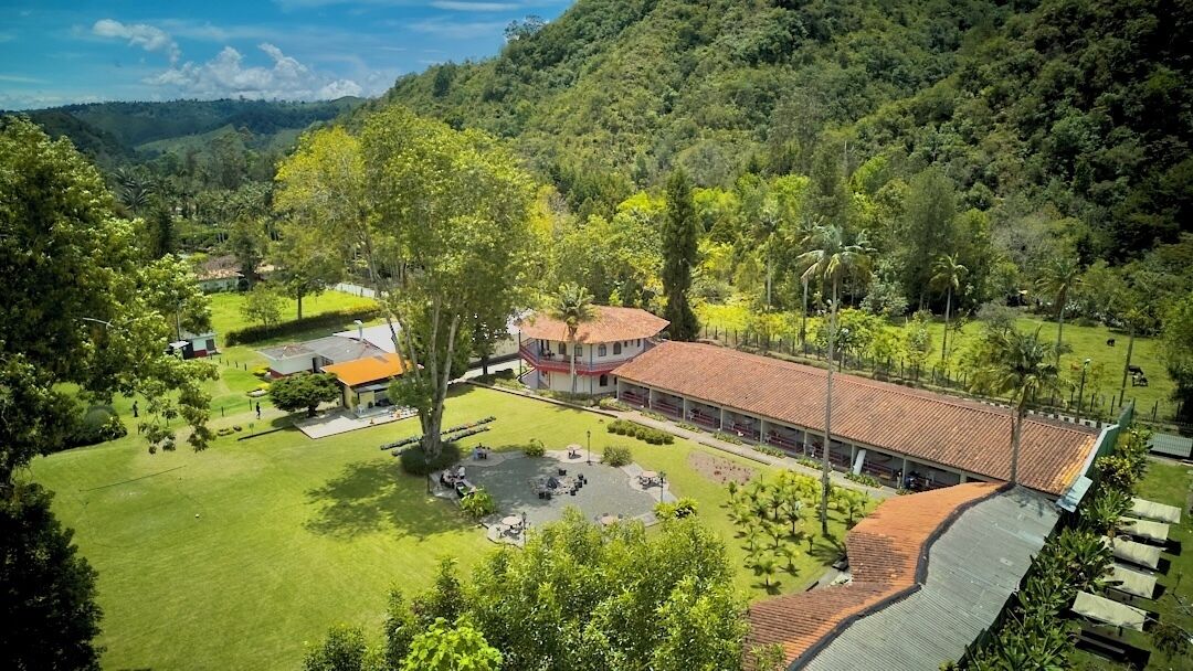 Um edifício grande com telhado vermelho, cercado por vegetação exuberante e um gramado bem cuidado.