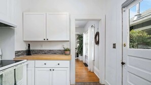 A narrow hallway with white cabinets, a wooden countertop, and a view into a room with a door and a wreath. - 3 BR 1 BA - Cozy Home - Walkscore 97 - Shopping (Portland)
