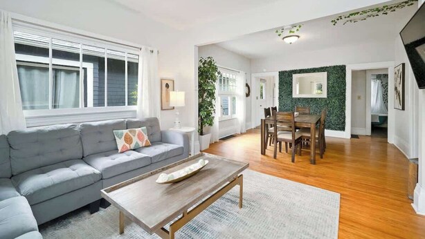 A modern living room with a grey sofa, wooden coffee table, and a dining area with a wooden table and chairs. - 3 BR 1 BA - Cozy Home - Walkscore 97 - Shopping (Portland)