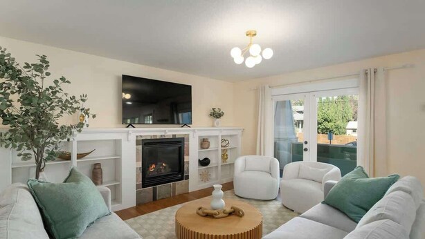 A living room with a fireplace, white sofas, a round coffee table, and a television mounted above the fireplace.