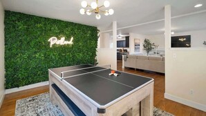 A ping pong table in a living room with a green wall and a neon sign that reads "Pool".