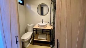 A compact bathroom with a toilet, a sink, and a mirror. - Casa Marina (Querétaro)